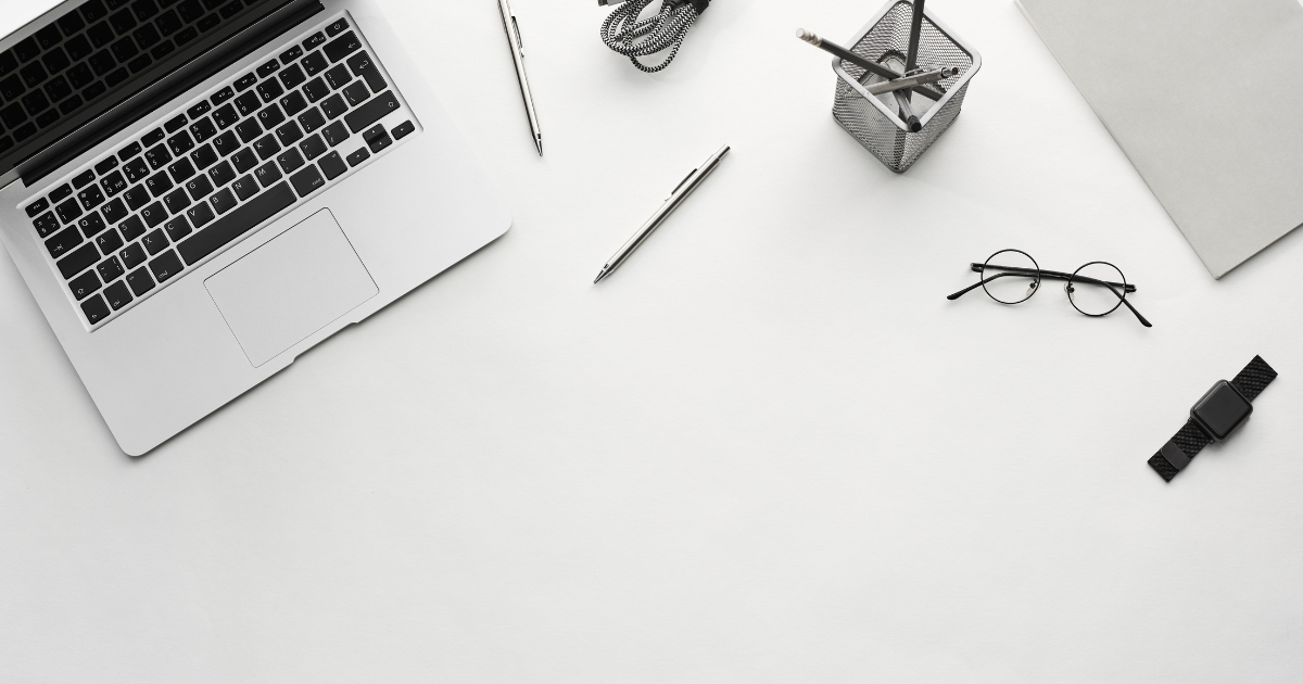 Overhead flat-lay of a laptop, notebook and accessories arranged on a clean white desk