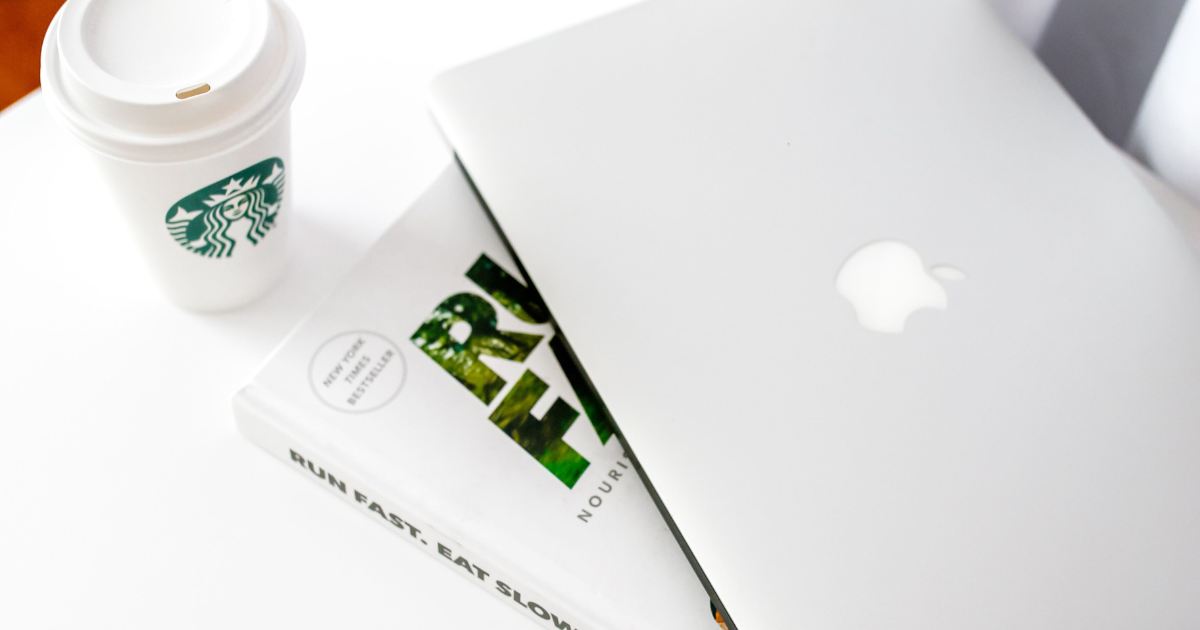 Overhead flat-lay of a laptop, open notebook and shopping bag arranged on a clean white surface